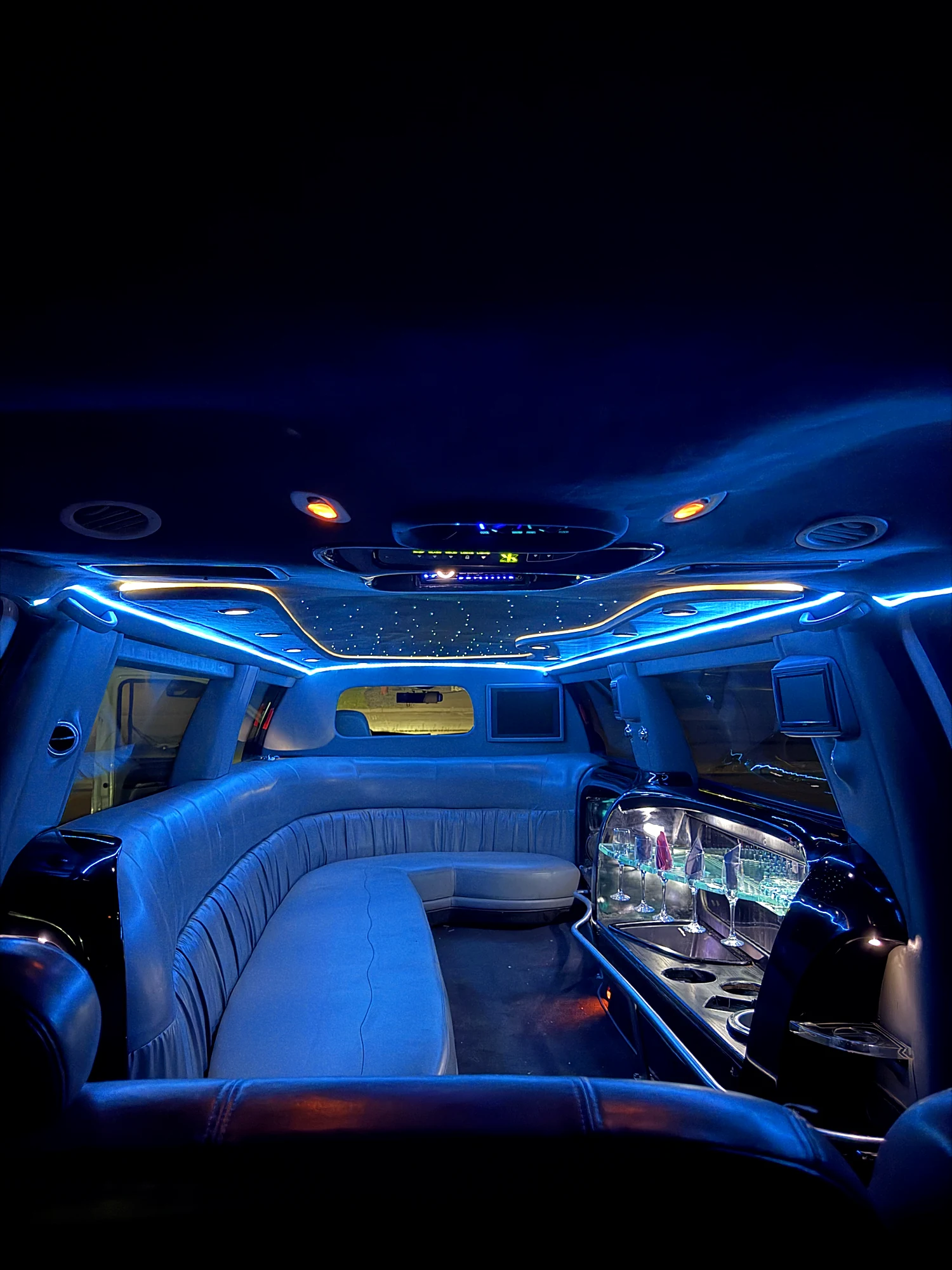 The stretch limousine cabin lit in blue, star ceiling above the bench and bar