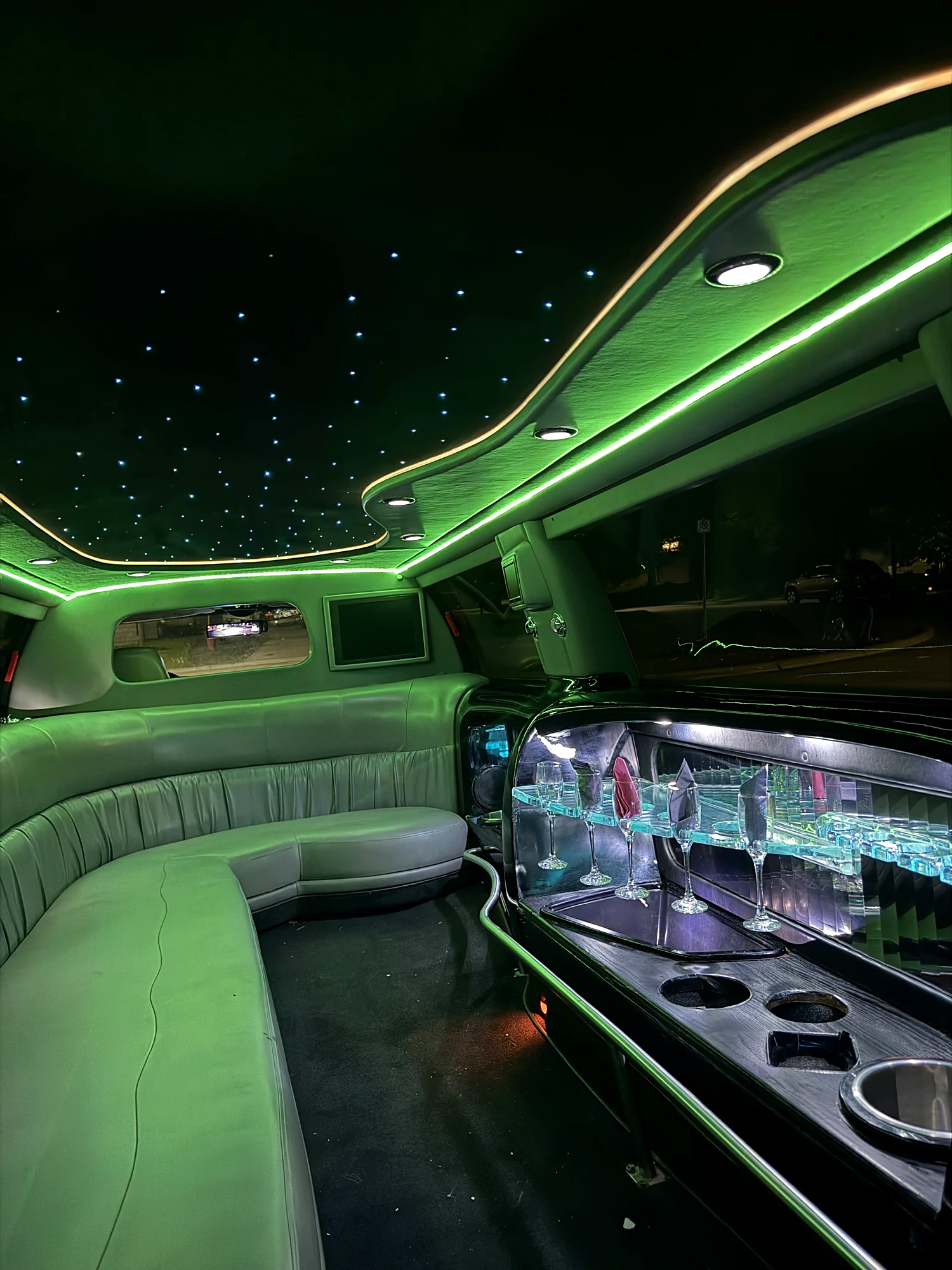 The stretch limousine cabin lit in green, star ceiling above the bench and bar