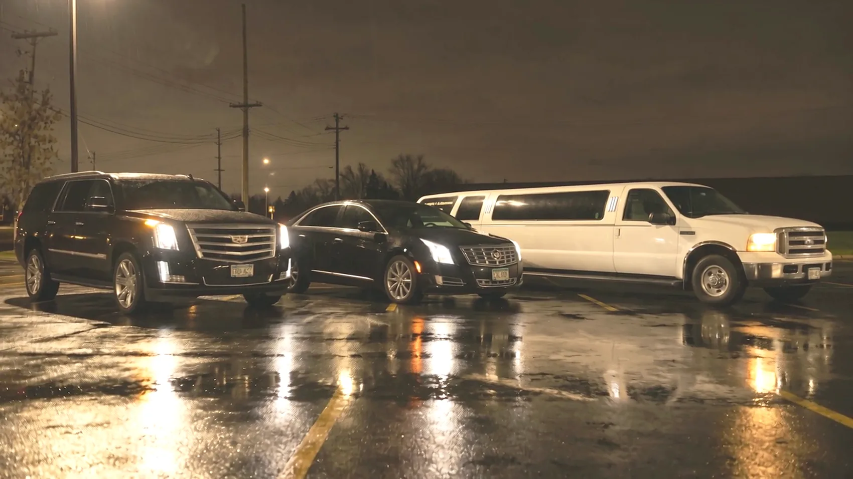 The Escalade ESV, Cadillac XTS and Excursion stretch limousine parked side by side on a wet lot at night